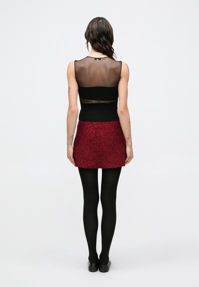 Czarny top bez rękawów z przezroczystymi panelami, zestawiony z czerwoną, teksturowaną mini spódnicą. Całość dopełniają czarne rajstopy i buty.