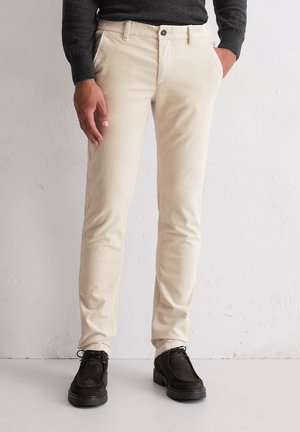 Beige Corduroyhose mit Slim-Fit, ausgestattet mit Vorderaschen und einem einzigen Knopfverschluss, kombiniert mit dunkelbraunen Wildlederschuhen.