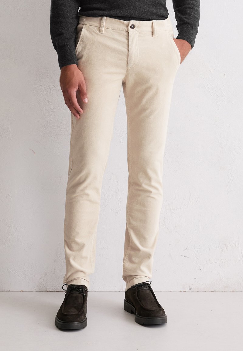 Beige corduroy broek met een slim fit, voorzien van zijzakken en een enkele knoopsluiting, gecombineerd met donker suède schoenen.