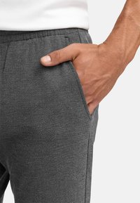 Pantalons texturés gris avec une poche latérale, une taille élastique et une coupe décontractée. Gros plan sur la taille et la position de la main.
