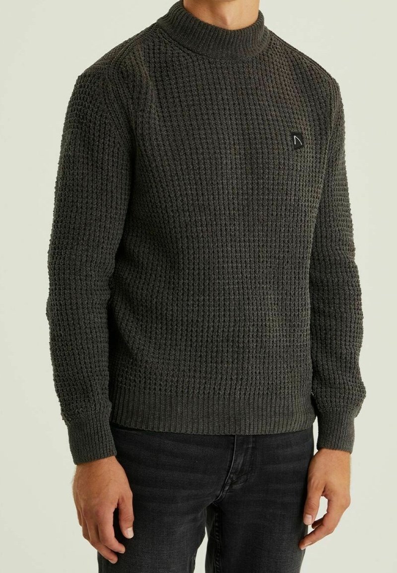 Gestrickter dunkelgrüner Pullover mit hohem Kragen, strukturiertem Muster, tailliertem Design und einem kleinen schwarzen Markenlogo auf der Brust.