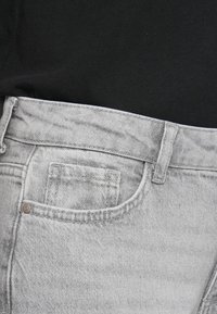 Gray denim jeans featuring a front pocket, stitched seam details, and a button closure at the waist, visible against a black shirt.