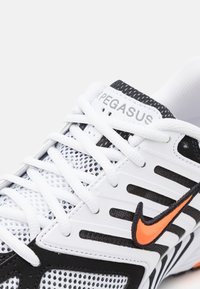 Gros plan de la chaussure de course Nike Pegasus blanche et noire avec le logo Swoosh orange et des lacets blancs sur une tige en mesh respirant.