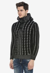 Schwarz- und grau gestreifter Pullover mit hohem Kragen, der ein Zopfmuster aufweist und ein Knopfdetail am Kragen hat.