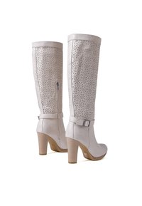 Stivali beige in faux leather al ginocchio con motivi floreali intagliati, zip laterale, dettaglio in cintura e tacco impilato.