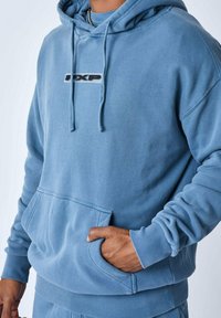 Sudadera de algodón azul con bolsillo canguro, puños y dobladillo acanalados, que presenta un pequeño logo negro en el pecho y un corte relajado.