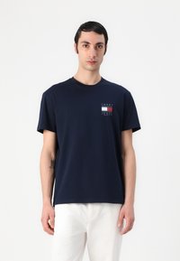 Marineblaue Baumwoll-T-Shirt mit einem kleinen grafischen Logo in Rot, Weiß und Blau auf der Brust, Rundhalsausschnitt und kurzen Ärmeln.