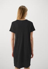 Černé šaty z tričkoviny vyrobené z měkkého materiálu, s krátkými rukávy, volným střihem a decentním detailem na zadním švu.