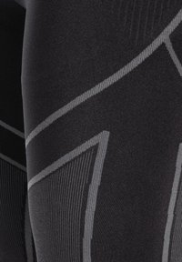 Czarne legginsy sportowe z teksturowanym wzorem i szarymi akcentami, wykonane z gładkiego materiału, o dopasowanym kroju podkreślającym kształt nóg.