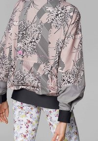 Bomber jacket floreale di un delicato rosa chiaro con motivo a righe, maniche grigie e polsini neri. Abbinala a leggings bianchi floreali per creare un contrasto.