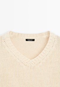 Pull en crème à col en V en tricot avec un motif texturé, des poignets côtelés, et une étiquette indiquant "Massimo Dutti, Fabriqué en Italie."