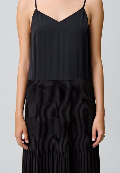 Vestito nero con top in satin e gonna plissettata, caratterizzato da un motivo ondulato. Spalline sottili e scollo a V. Texture liscia in tutto il capo.