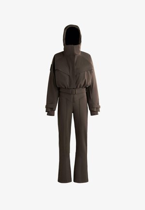 Hnedý overal s kapucňou, ktorý má opasok v páse, široké nohavice a význačné diagonálne švy na hrudi a nohaviciach.