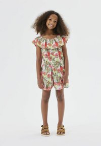 Combinaison florale en tissu léger avec des manches à volants, ornée de motifs tropicaux roses et verts, associée à des sandales à lanières marron.