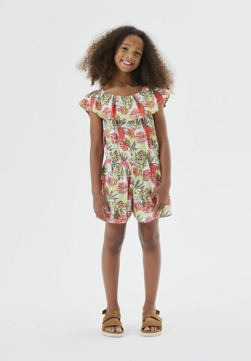 Combinaison florale en tissu léger avec des manches à volants, ornée de motifs tropicaux roses et verts, associée à des sandales à lanières marron.