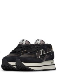 Scarpe da ginnastica atletiche nere e grigie realizzate in suede e mesh, con una suola bianca a contrasto, un design dei lacci prominente e un logo sulla linguetta.