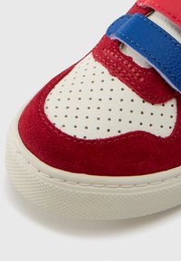 Rød semsket joggesko med hvit perforert lærtå, blå borrelåsstropp og teksturert gummisåle. Særpreget sømdetalj på overdelen.