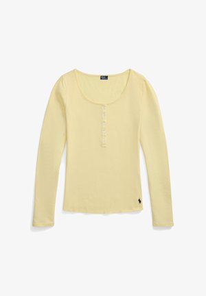 Světlounce žluté tričko s dlouhým rukávem typu henley s výstřihem do lodi, se šesti knoflíky vpředu a malým černým vyšívaným logem poblíž spodního lemu.
