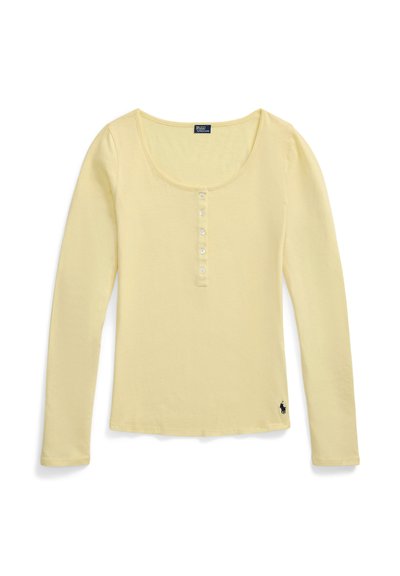 Chemise henley à manches longues jaune clair avec encolure dégagée, six boutons sur le devant et petit logo noir brodé près de l'ourlet inférieur.