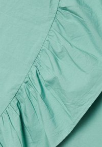 Tecido azul-petróleo claro com uma voluta franzida ao longo de uma borda, apresentando uma textura suave e mínimas rugas.