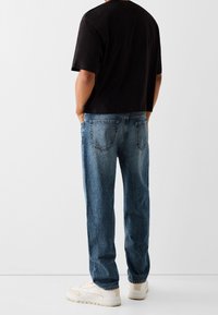 Svart t-shirt med kort ärm, ljusblå jeans i denim med avslappnad passform och beigea sneakers. Enkel design, standardstygn och två bakfickor.