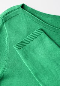 Vihreä neulepaita, jossa on pyöreä pääntie ja ribbauslahkeet. Pintakuvio on sileä ja tasainen matta viimeistely.