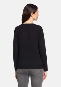 Pull noir à manches longues avec un col rond, un ourlet côtelé et une texture lisse. Le modèle porte un jean gris avec des poches arrière visibles.