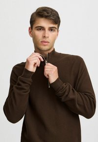 Brown textured pullover with a high collar and a half-zipper. Features fitted long sleeves and a honeycomb pattern throughout.