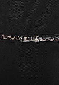 Sort beklædningsgenstand med tekstureret overflade, snøret ind med et leopardmønstret bælte og en sølvfarvet metalspænde.