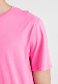 Trumpomis rankovėmis marškinėliai ryškiai rožinės medvilnės, su apvalia iškirpte ir lygiu paviršiumi. Rankovėse matyti siūlių detalės.