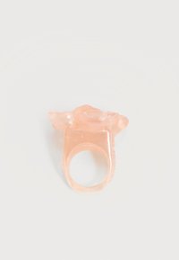 Anillo de plástico rosa translúcido con una decoración en forma de rosa en la parte superior, mostrado sobre un fondo blanco liso.