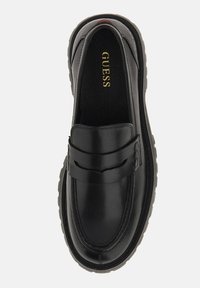 Black leather loafers with a smooth texture, featuring a stitched design and a rubber sole. Gold "GUESS" logo is visible on the insole.