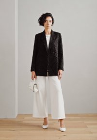 Svart sammetsblazer med zebramönster, parat med en vit topp och vida vita byxor. Accessoarer med en liten vit handväska och klackar.