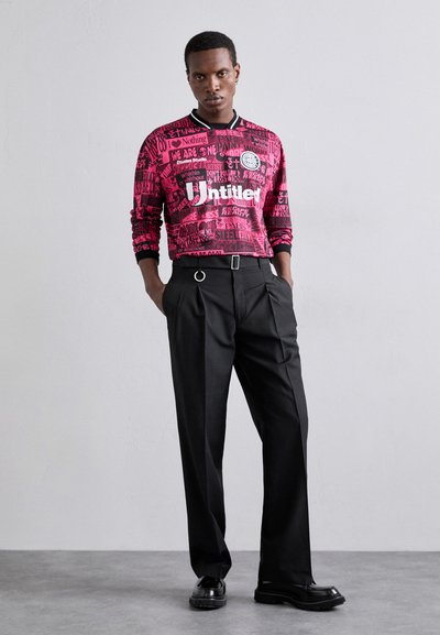 Long-sleeve pink graphic t-shirt with black text, paired with black trousers featuring a belt and metal ring detail. Black platform shoes.
