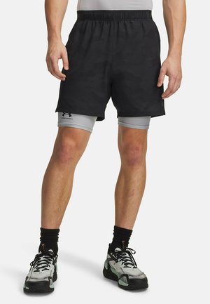 Hombre que lleva pantalones cortos deportivos negros con mallas de compresión grises debajo y calcetines negros con zapatos deportivos grises.