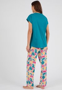 Turkooise t-shirt met korte mouwen gecombineerd met bloemenpatroon, losse broeken in roze, groen en geel op een lichte achtergrond.