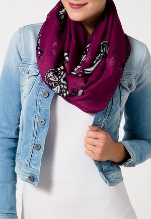 Femme portant une écharpe infinie violette avec des motifs de papillons noirs et blancs portée sur une veste en jean claire et un haut blanc.