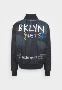 Veste bomber noire avec le texte "BKLYN NETS", la silhouette du pont de Brooklyn, et les détails "Brooklyn New York" au dos.