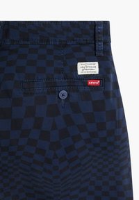 Tummansiniset ruudulliset housut, joissa on sileä rakenne, takatasku, nappikiinnitys ja Levi's -merkki ommeltuna vyötärönauhaan.