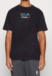T-shirt noir en coton à coupe décontractée, ornée d'une broderie multicolore du logo "NBA BASKETBALL" sur la poitrine. Manches courtes et col rond.
