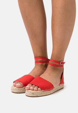 Sandalias espadrilles rojas con diseño de punta abierta, parte superior de lona y dos correas en el tobillo, con suela de yute trenzada y textura suave.