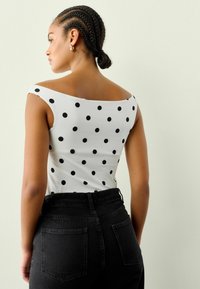 Biała bluzka w czarne kropki, projekt bez ramiączek, w połączeniu z czarnymi dżinsami o wysokim stanie. Posiada gładką teksturę materiału.