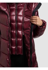 Bordós krūmains mētelis ar sutinātu faktūru, kuram priekšā ir rāvējslēdzējs un melni akcenti malās. Iekšējā kārta arī ir sutināta.