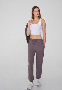 Pantalones de chándal grises con cintura elástica y cordones, combinados con un top corto blanco. La modelo lleva zapatillas blancas. Corte simple y relajado.