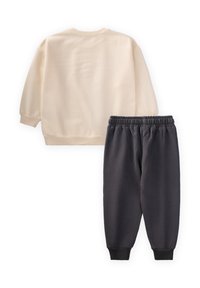Cream sweatshirt with long sleeves and a rounded neckline, paired with dark gray sweatpants featuring an elastic waistband and cuffed ankles.