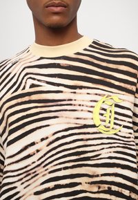 Svart och tan randig sweatshirt med en gul broderad "G"-logotyp på vänster sida och en krämfärgad ribbad halsringning.