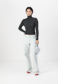 Suéter de cuello alto acanalado gris, jeans de pierna ancha azul claro, zapatos rojos y blancos, sosteniendo un bolso plateado. Diseño simple y ajustado con textura.