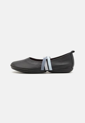 Zapatos planos de piel negra con punta redonda, suela flexible y dos bandas elásticas decorativas en azul claro y gris.