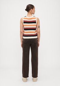 Top senza maniche a righe in arancione, bianco e nero; abbinato a pantaloni larghi marroni e sneakers beige. La vista posteriore mostra i dettagli sulle spalle.