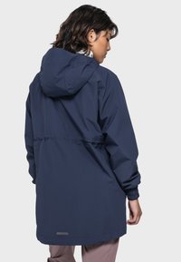 Marineblauer wasserdichter Jacke mit Kapuze, elastischen Bündchen und verstellbarem Bund; glatte Textur und minimalistisches Design mit einem reflektierenden Detail.